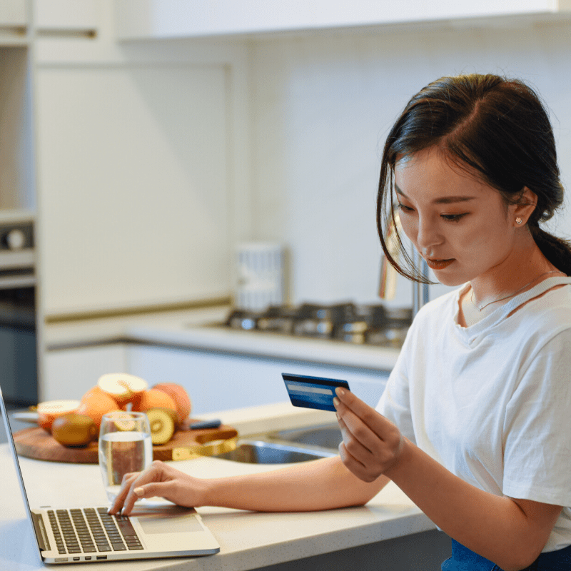 Woman online shopping on a laptop with credit card at her kitchen bench